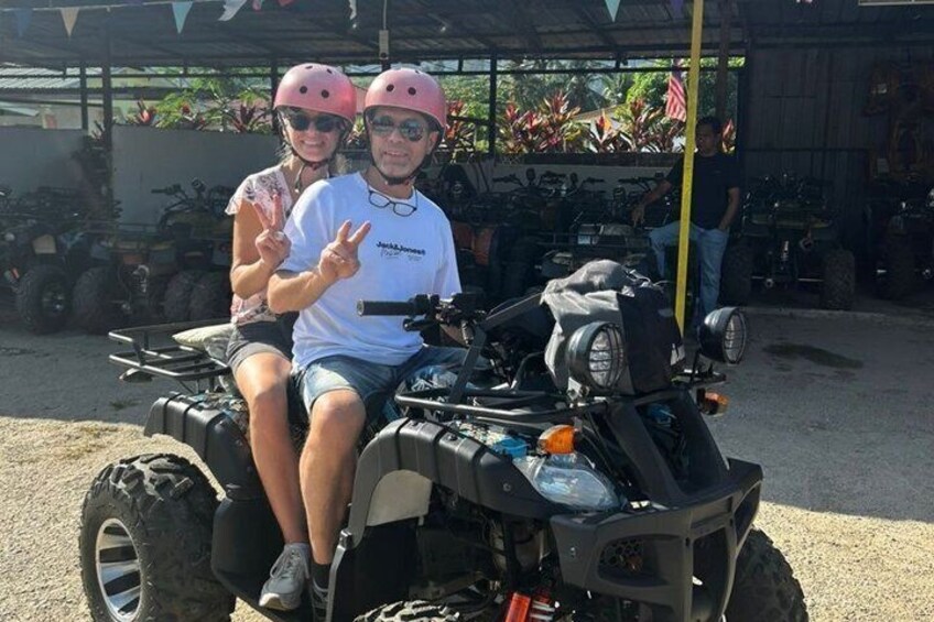 Two people on an ATV with helmets, a white t-shirt, and a peace sign. 1