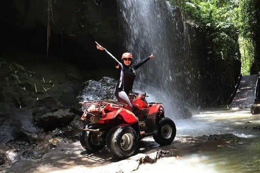 A person on a red ATV in a forested area with a waterfall. 2