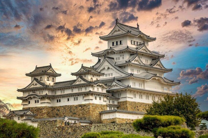 A traditional Japanese castle with multiple tiers and a stone base, surrounded by greenery. 1