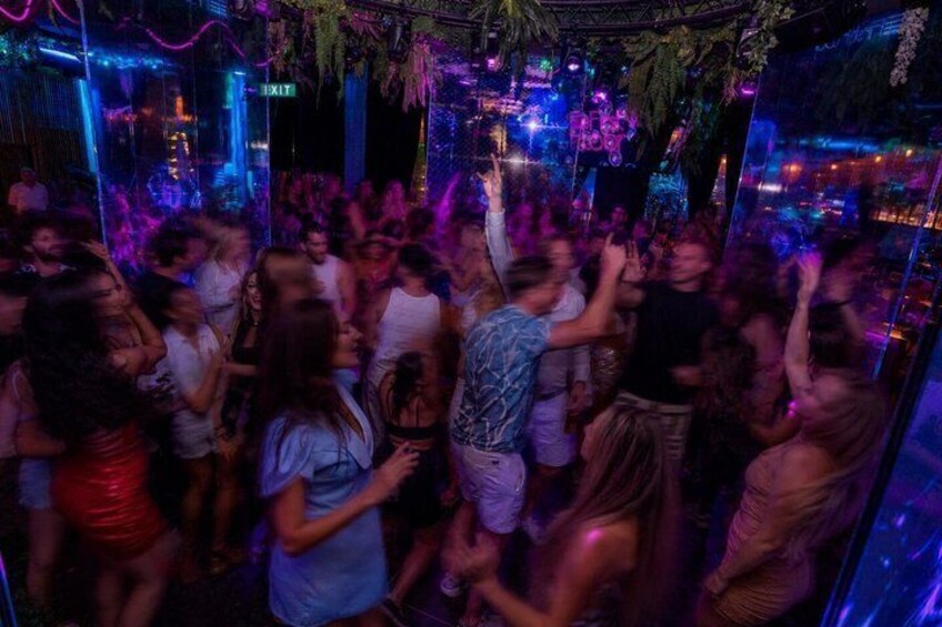 A crowded indoor venue with people dancing, neon lights, and a DJ booth. 5