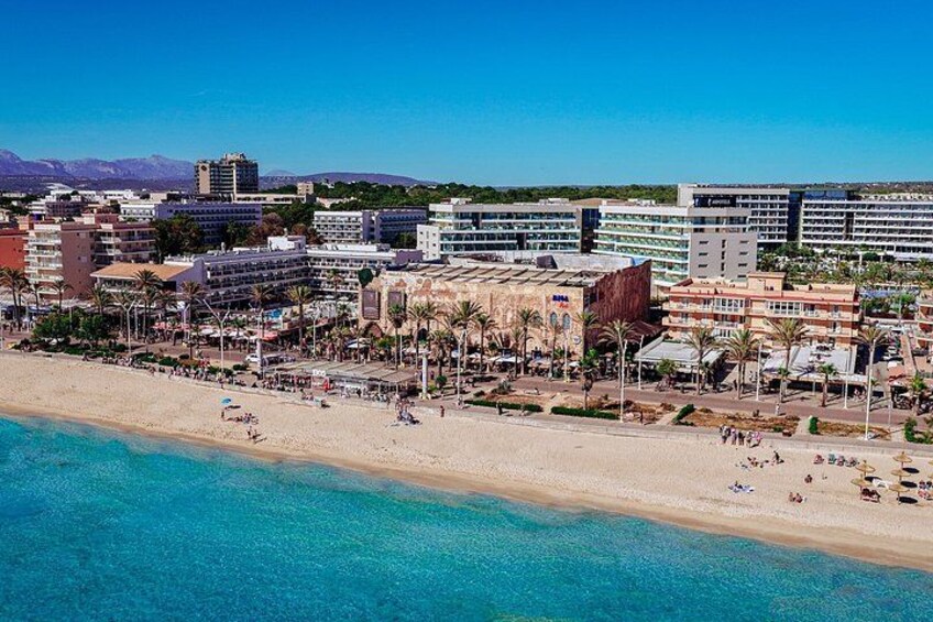 A coastal cityscape with a beach, buildings, and clear blue waters. 2
