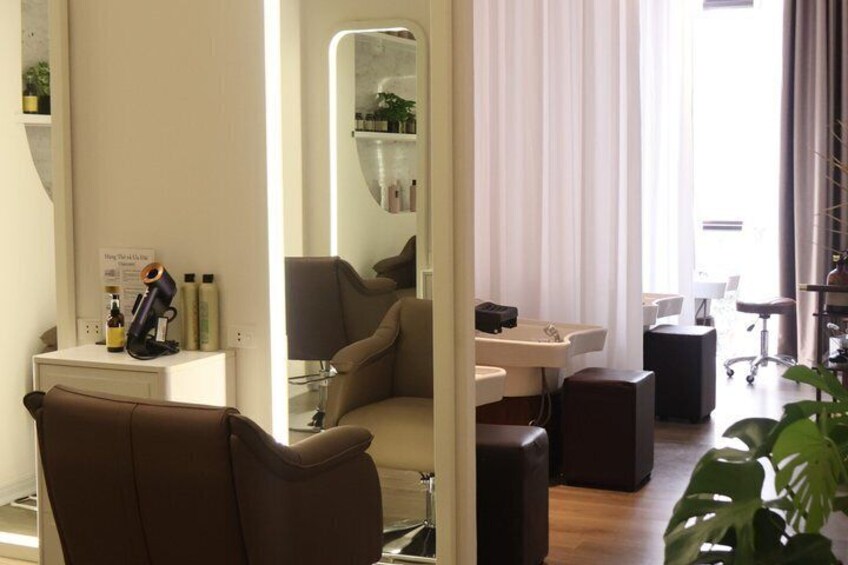 A salon interior with a mirror, chairs, a desk, and a plant. 5