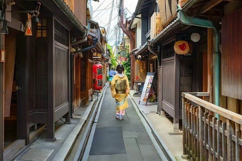 A narrow street with traditional wooden buildings, a red fire hydrant, and a person in traditional attire walking down the path. 3