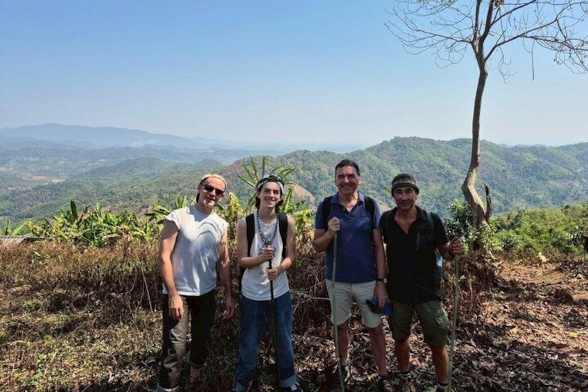 Three people standing on a hill with a mountainous landscape in the background. 1