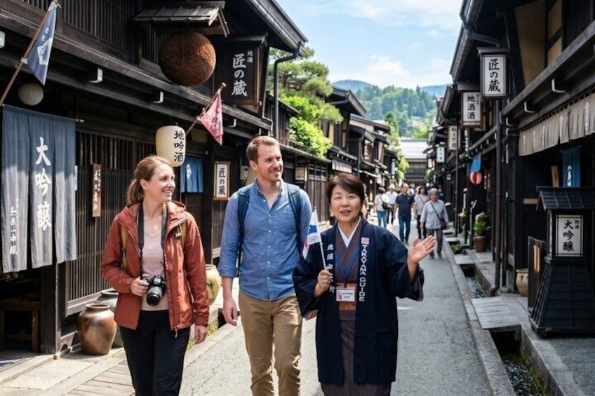 A narrow street lined with traditional wooden buildings, a camera, and a person gesturing. 1