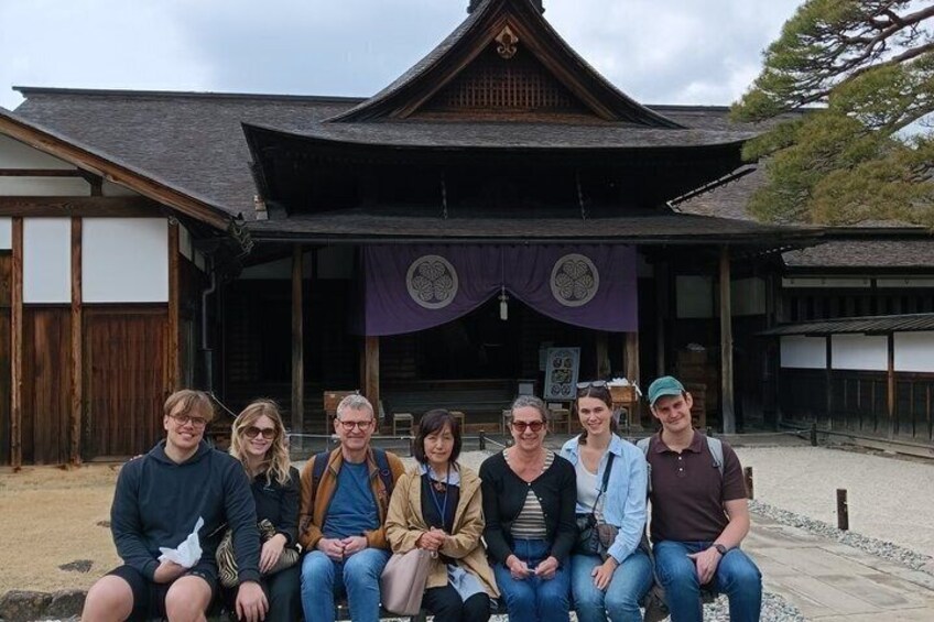 A group of people seated in front of a traditional Japanese building with a tiled roof and wooden structure. 4