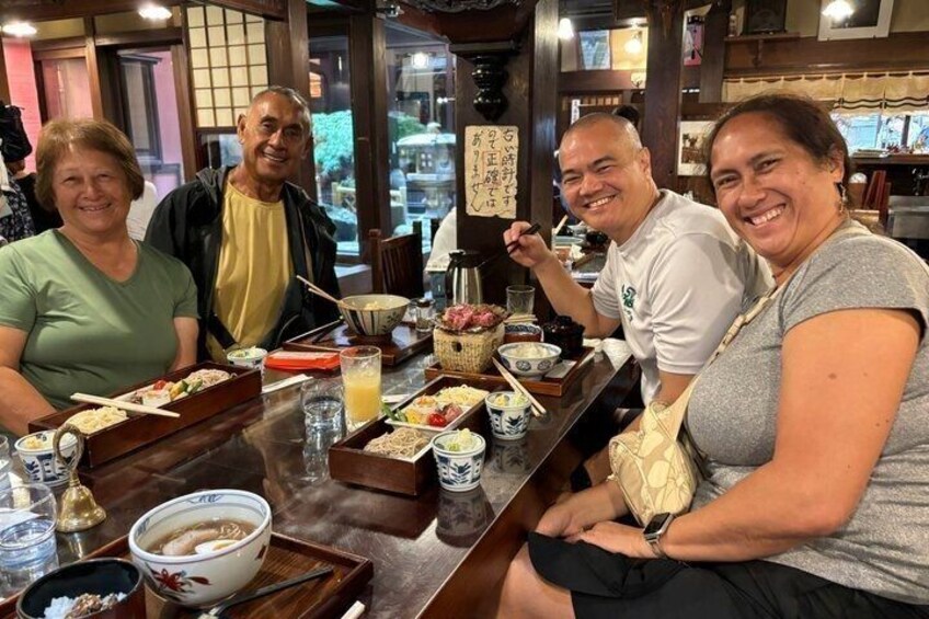 A group of people sitting at a table with various dishes and drinks, in a restaurant with traditional decor. 5