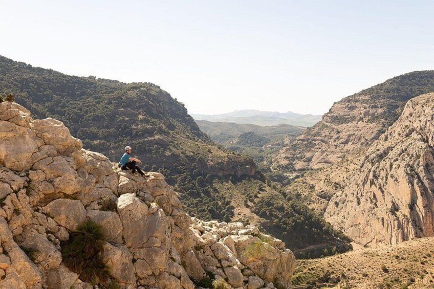 A person sitting on a rocky outcrop overlooking a valley with mountains in the background. 5