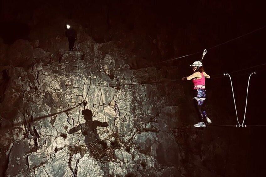 A person performing a zip-lining activity in a rocky outdoor setting at night. 2