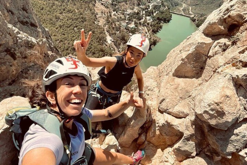 Two people rock climbing on a cliff with a valley and lake in the background. 1