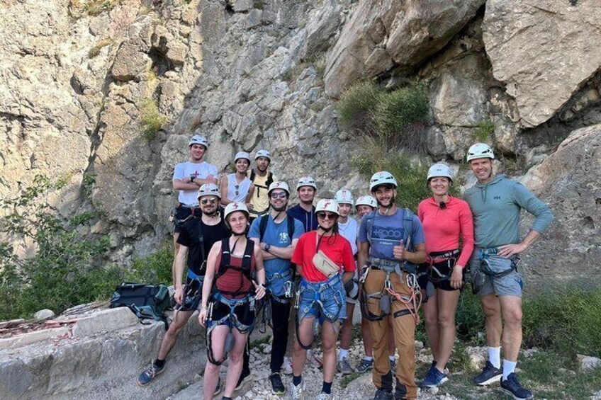 A group of people with helmets and harnesses, standing on a rocky cliff. 5