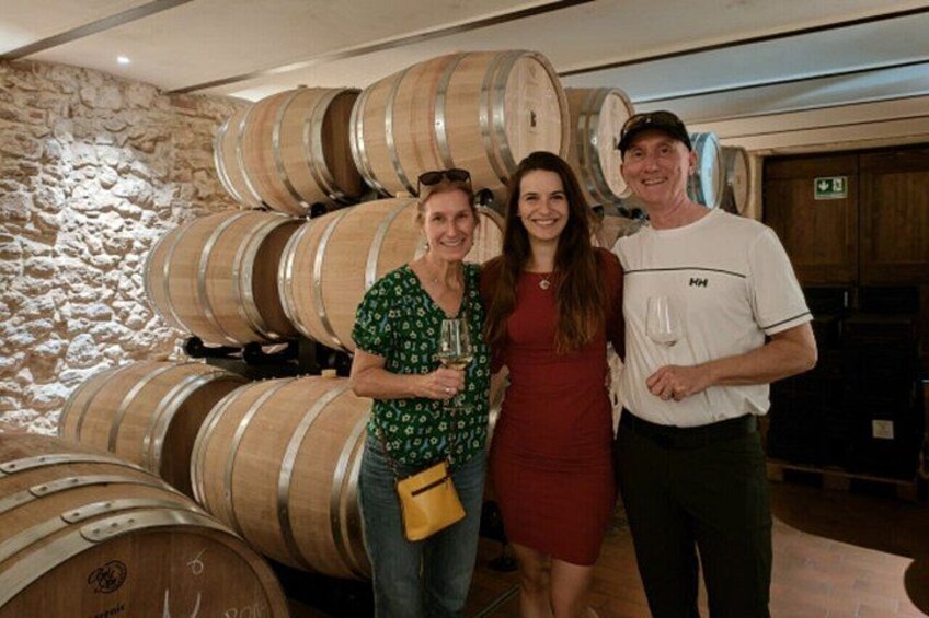 Three people standing in front of large wooden wine barrels. 4