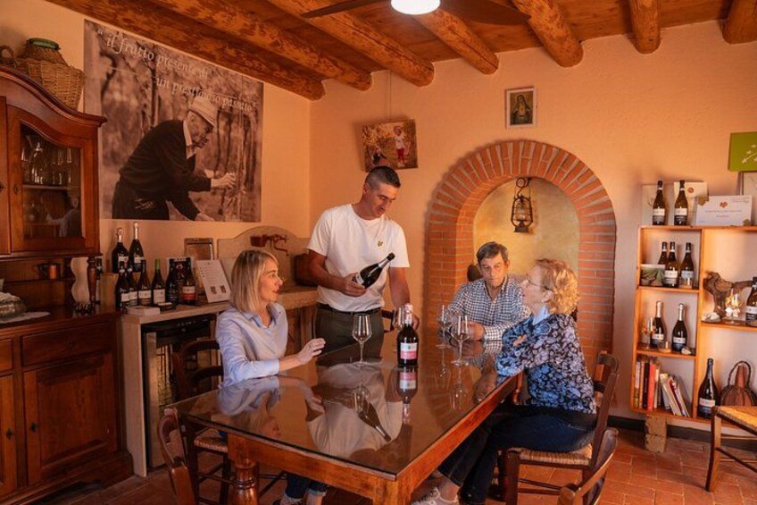 A rustic wine cellar with wooden shelves, a brick archway, and a glass-topped table where people are tasting wine. 3
