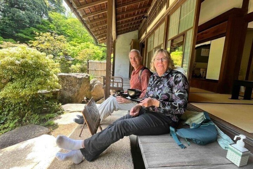 Two people sitting on a wooden bench outdoors, with a traditional Japanese building in the background. 1