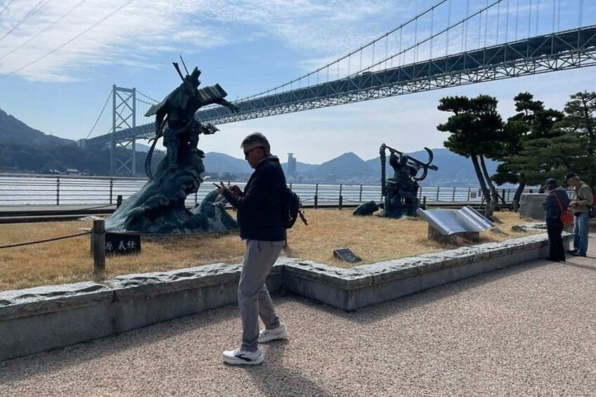A person standing near a sculpture, a bridge, and a body of water. 2