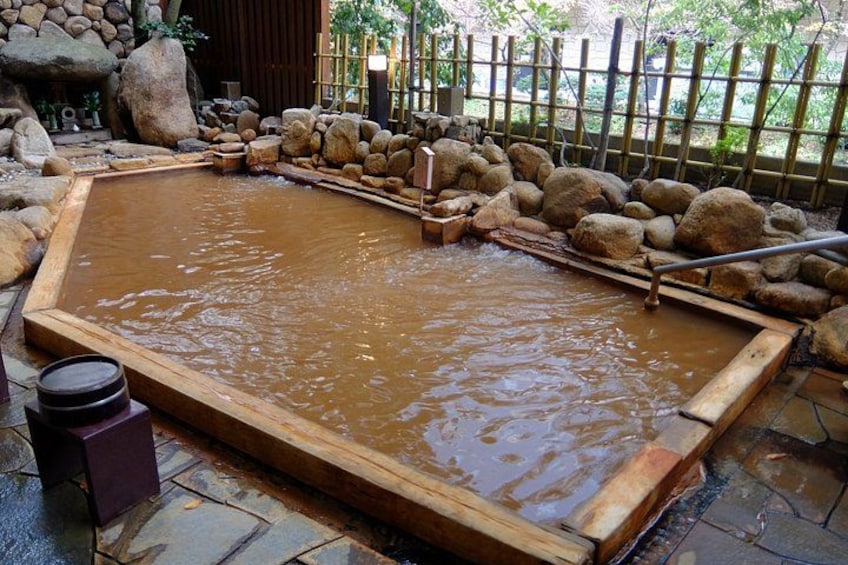 A traditional Japanese onsen with a wooden bath surrounded by rocks and a bamboo fence. 1
