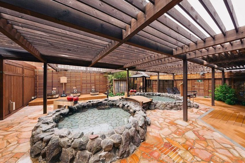 A traditional Japanese garden with stone hot springs, wooden structures, and a wooden pergola. 5