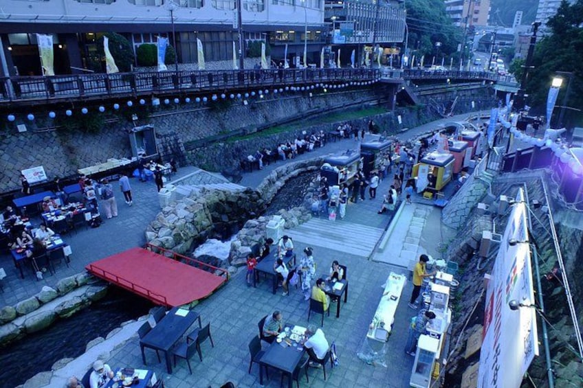 A riverside market with stalls and tables, a red-roofed structure, and a stone embankment. 2