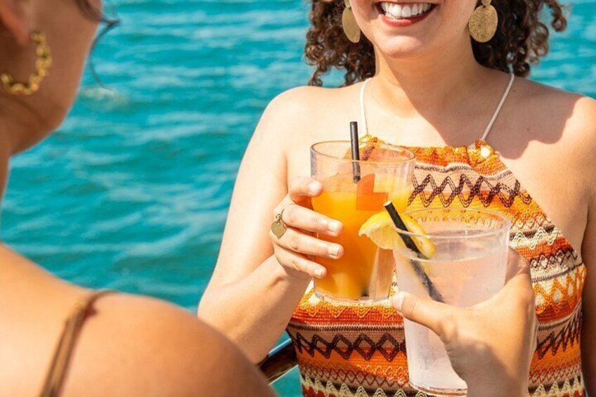 A person holding a glass with a straw and a slice of lemon, wearing a patterned top, with a body of water in the background. 2