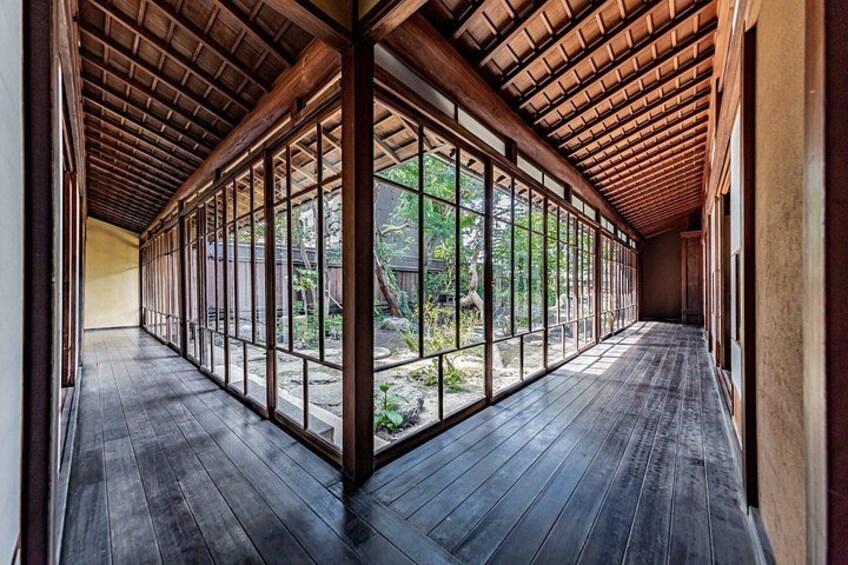 A corridor with wooden flooring and a tiled ceiling, leading to a garden with a wooden fence. 2