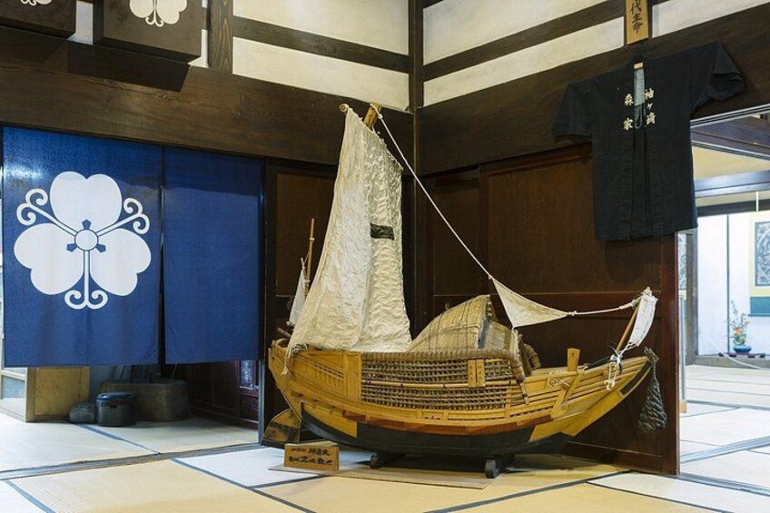 A traditional Japanese boat model displayed indoors, with tatami mats on the floor and a blue and white wall with a floral design. 4