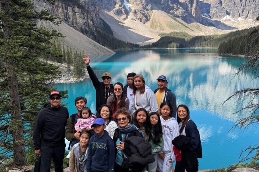 A group of people posing in front of a mountain lake with clear blue water and surrounding rugged mountains. 1