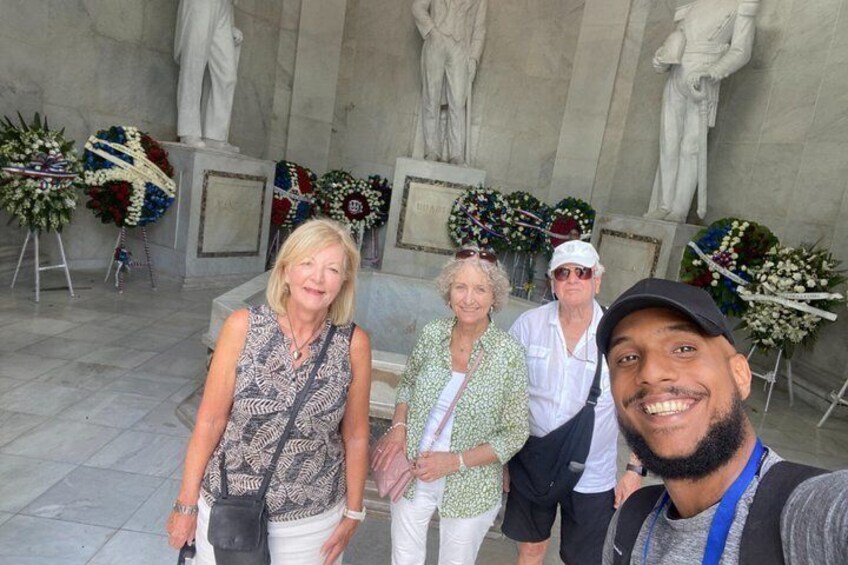 A group of people standing in front of a memorial with statues and floral arrangements. 5