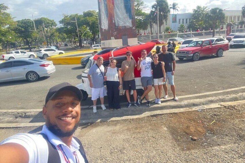 A group of people standing on a street with a red car and a yellow taxi in the background. 4