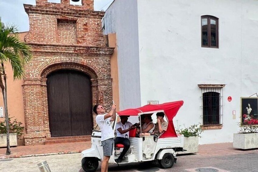 A white and red car with passengers, parked in front of a brick building with a large door. 3