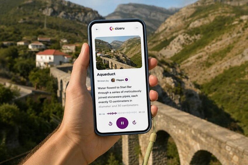 A hand holding a smartphone displaying a photo of a stone aqueduct with a caption. 1