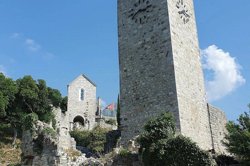 A stone tower with a clock, ruins, and a church in the background. 5