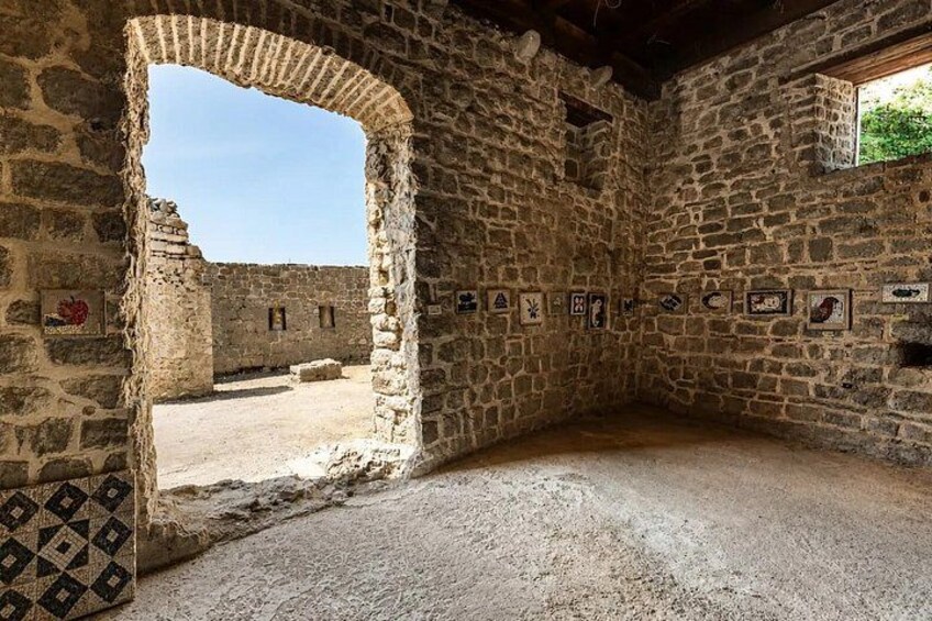 A stone-walled room with a large arched doorway leading outside, a tiled floor, and several framed pictures on the wall. 2
