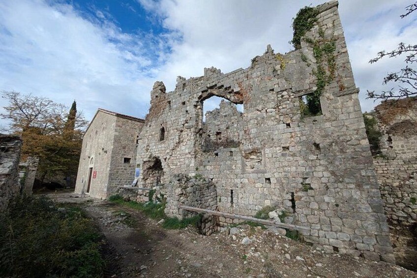 A historic stone building with ruins, a path, and a tree. 3