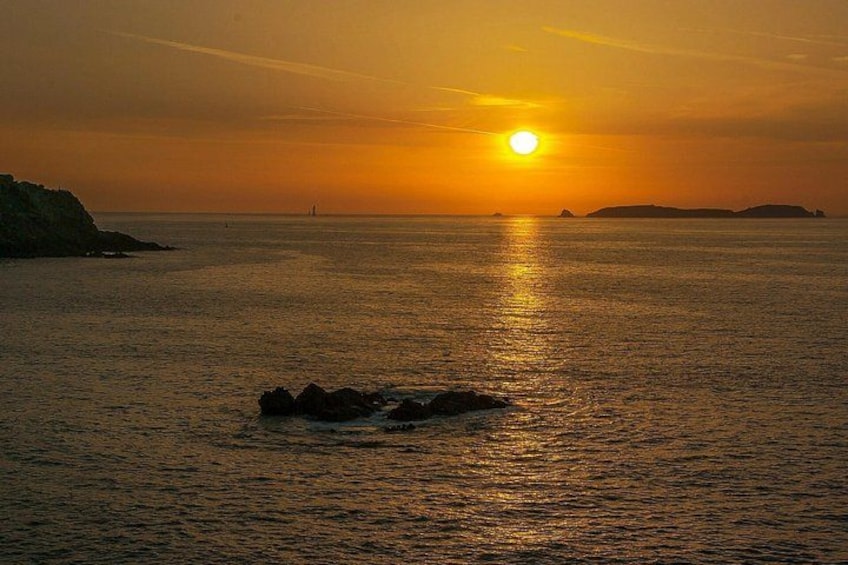 A sunset over a calm sea with a rocky outcrop in the foreground. 5