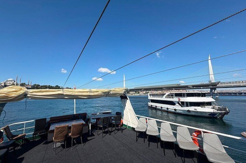 A boat deck with chairs and a dining area, a large white boat, and a cable-stayed bridge in the background. 3