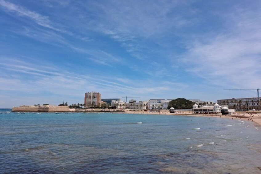 A coastal cityscape with a clear sky, a sandy beach, and a prominent building with a dome structure. 4