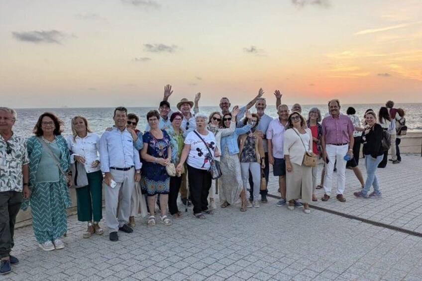 A group of people standing on a waterfront promenade during sunset. 2