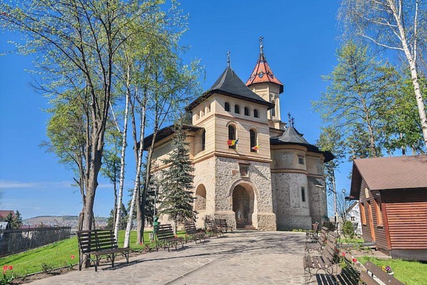 A historic church with a bell tower, surrounded by trees and benches. 3