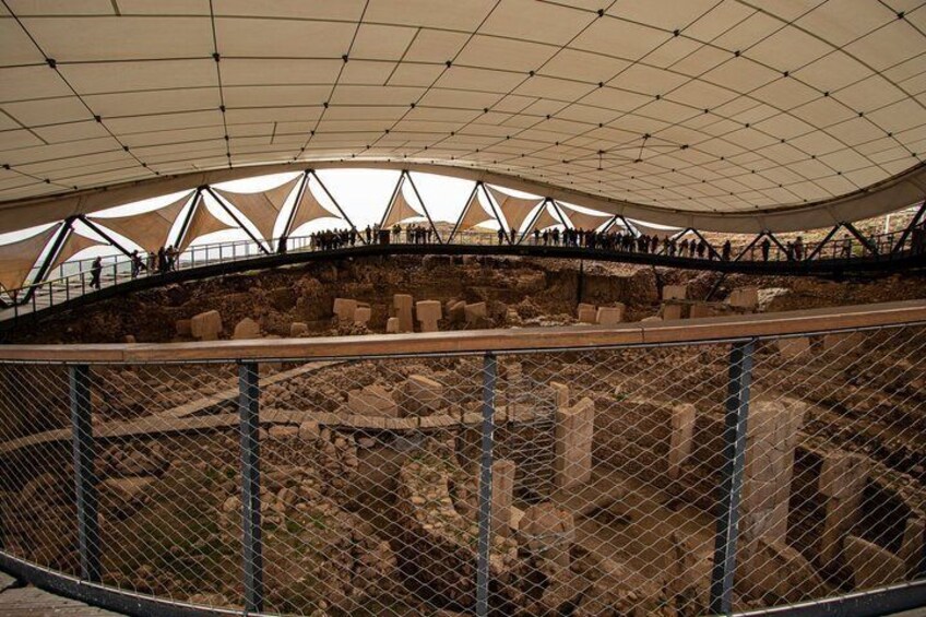 An archaeological site with a large open-air structure and a walkway above the ruins. 2