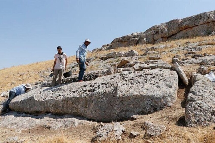 A group of people on a rocky hillside, some standing and others working on the ground. 5