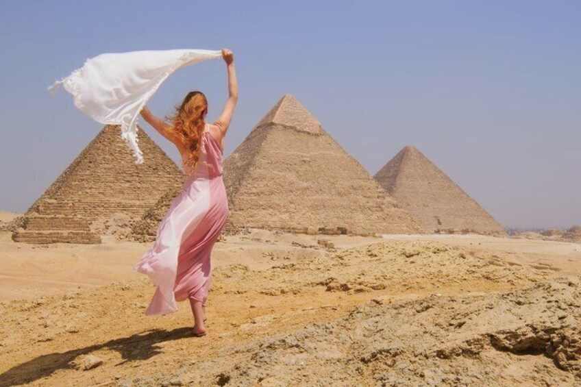 A person in a pink dress standing in front of the Great Pyramids of Giza. 2