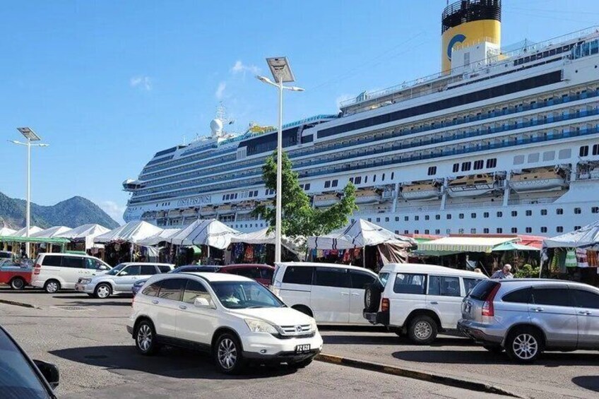 A cruise ship docked at a port with cars and market stalls in the foreground. 4