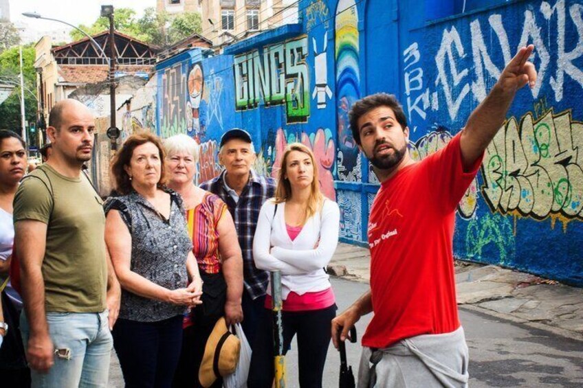A group of people standing in front of a graffiti-covered wall with the word 'GINE' visible. 5