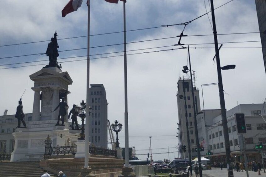 A statue of a historical figure on a pedestal, surrounded by steps, with buildings and a traffic light in the background. 3