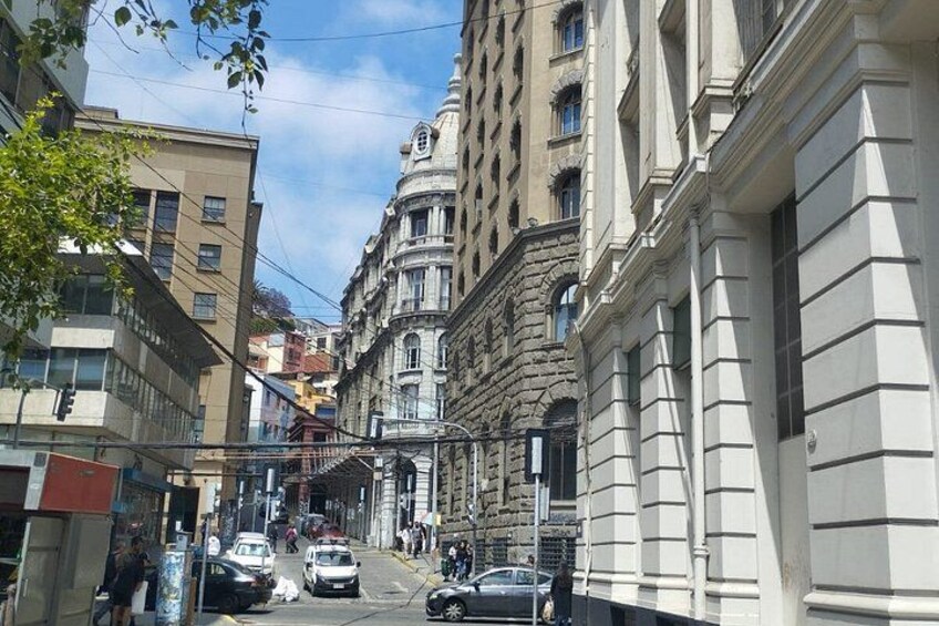 A street with historic buildings, cars, and pedestrians. 2