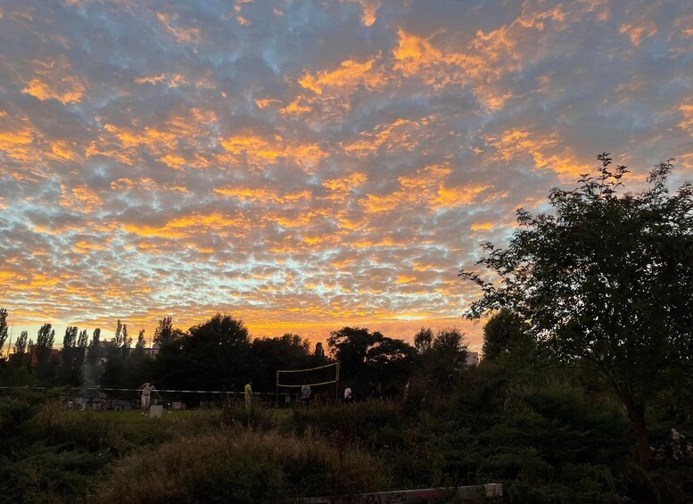 A sunset with a sky filled with orange and yellow clouds, trees, and a volleyball net in the foreground. 2