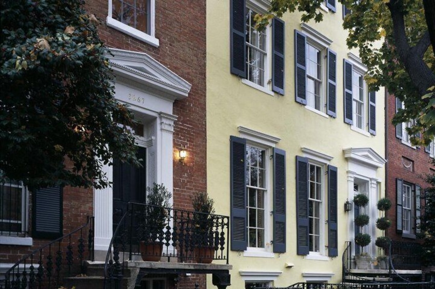 A row of colorful townhouses with black shutters, a brick building, and a tree in the foreground. 3