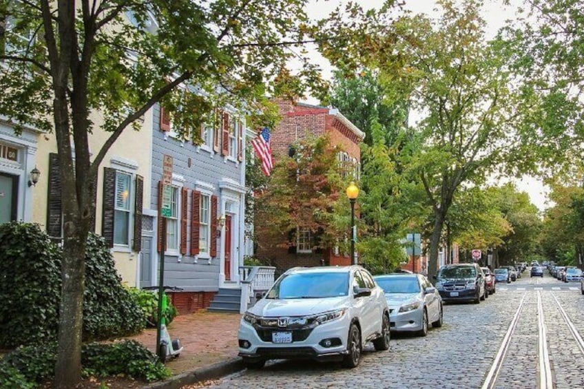 A cobblestone street lined with historic buildings, a tram track, and parked cars. 5