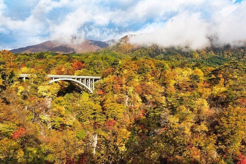 A bridge over a forested area with autumn foliage, a mountain in the background, and clouds. 3