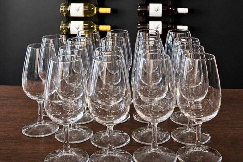 A collection of empty wine glasses arranged on a table with wine bottles in the background. 4